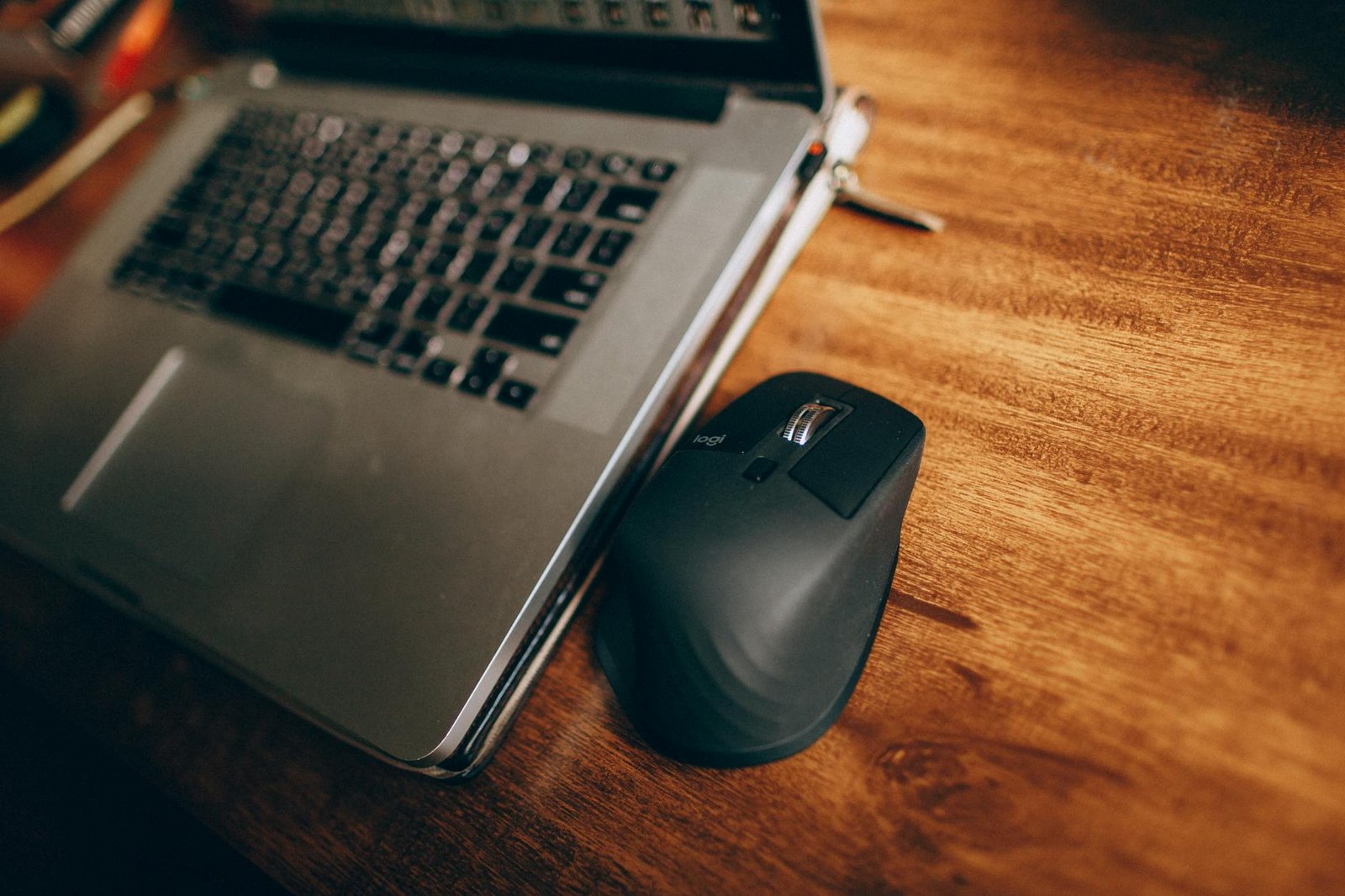 Close-up of a wireless mouse and laptop on a wooden desk, ideal for tech and workspace concepts.